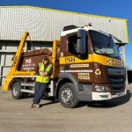 Smiling man standing by a PSH truck outside against blue sky